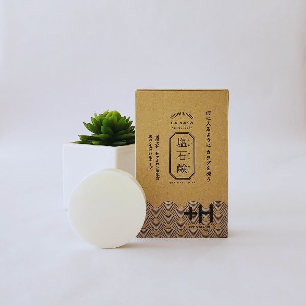 Salt Soap + Hyaluronic Acid Soap bar displayed in front of its box, complemented by a white pot and green plant on a white background