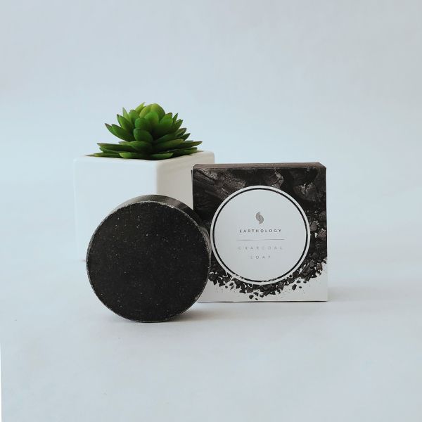 Charcoal Soap with Sea Salt displayed in front of its box, with a white pot and green plant on a clean white background