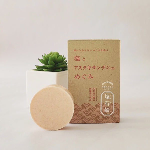 Salt and Astaxanthin Soap bar in front of its packaging with a small white pot and green plant on a white background